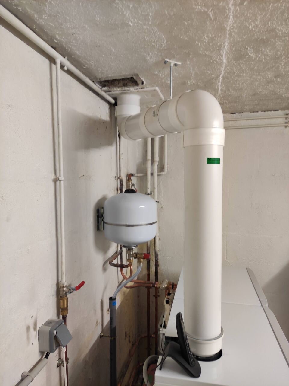 Le conduit d'évacuation blanc de la chaudière, qui prend deux coudes à angle droit avant de traverser le plafond.