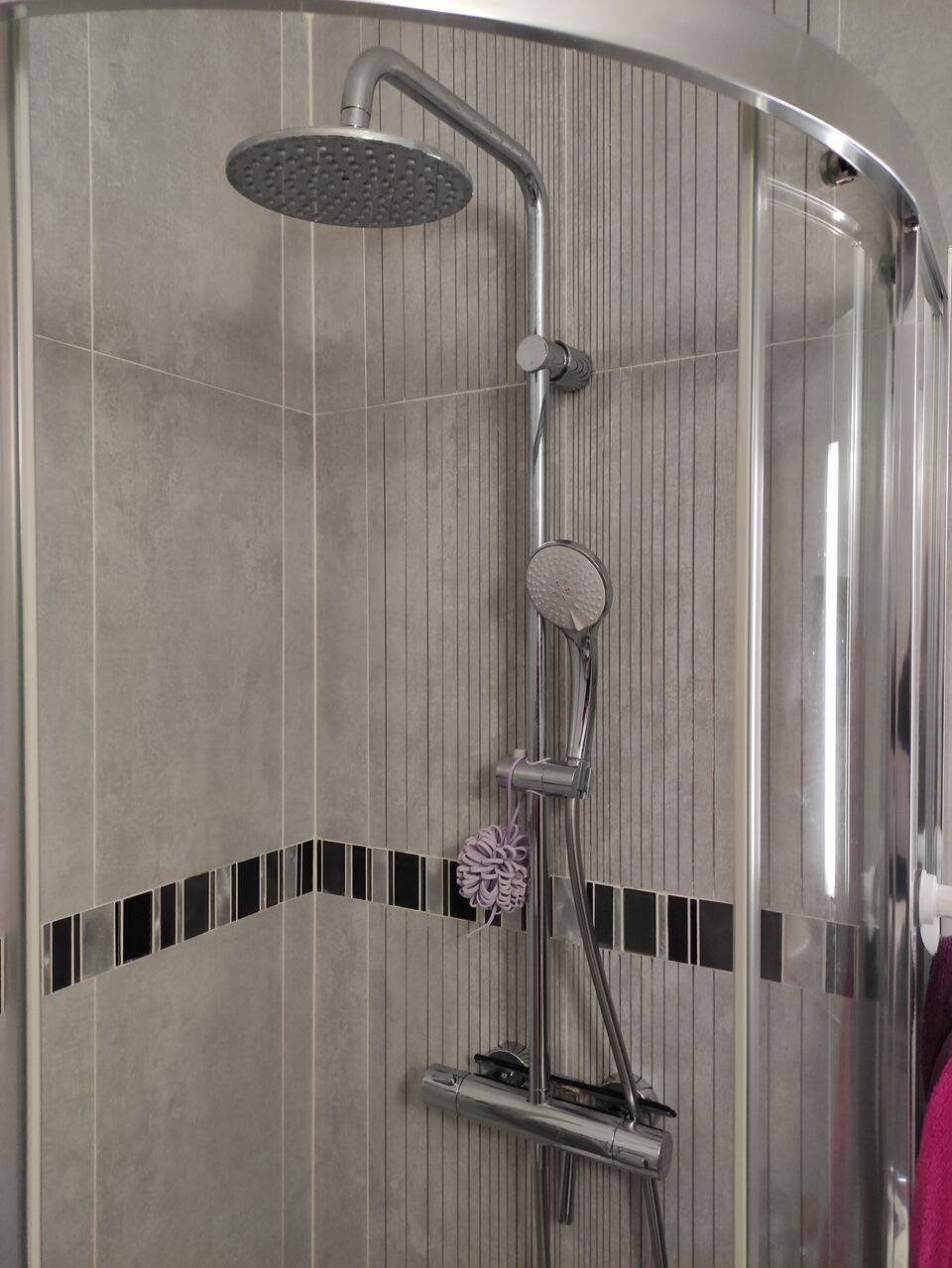 Colonne de douche chromée à mitigeur thermostatique, avec ciel de pluie et douchette, installée dans une cabine d'angle carrelée.