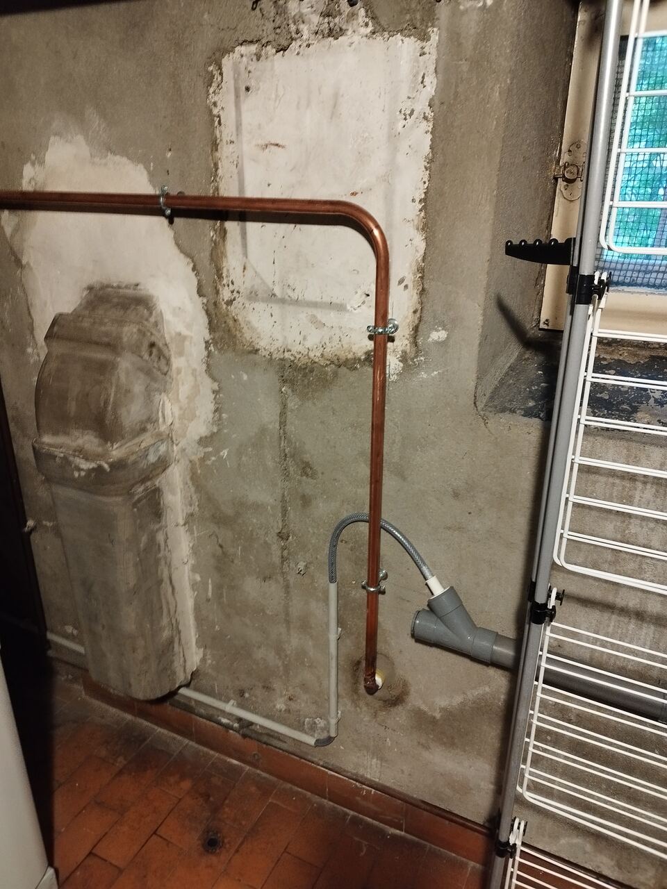 Mur de cave repris au plâtre après dépose, avec un tube cuivre neuf coudé à angle droit et une évacuation de condensats en attente.